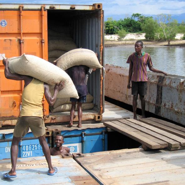 People loading sacks into a shipping container by a body of water.