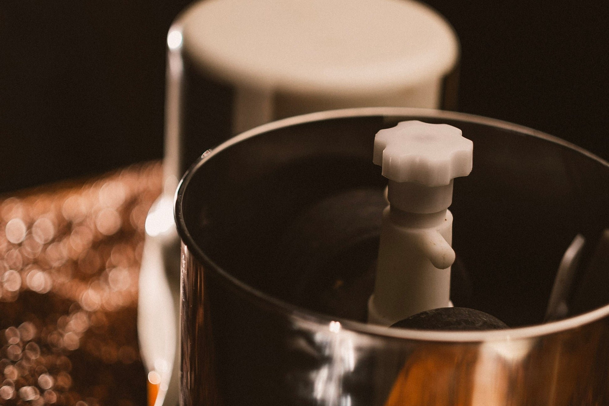 A close-up shot of the Spectra 11 Chocolate Melanger, featuring a white base, stainless steel bowl, and orange power button, set against a bed of cacao beans with warm, moody lighting.