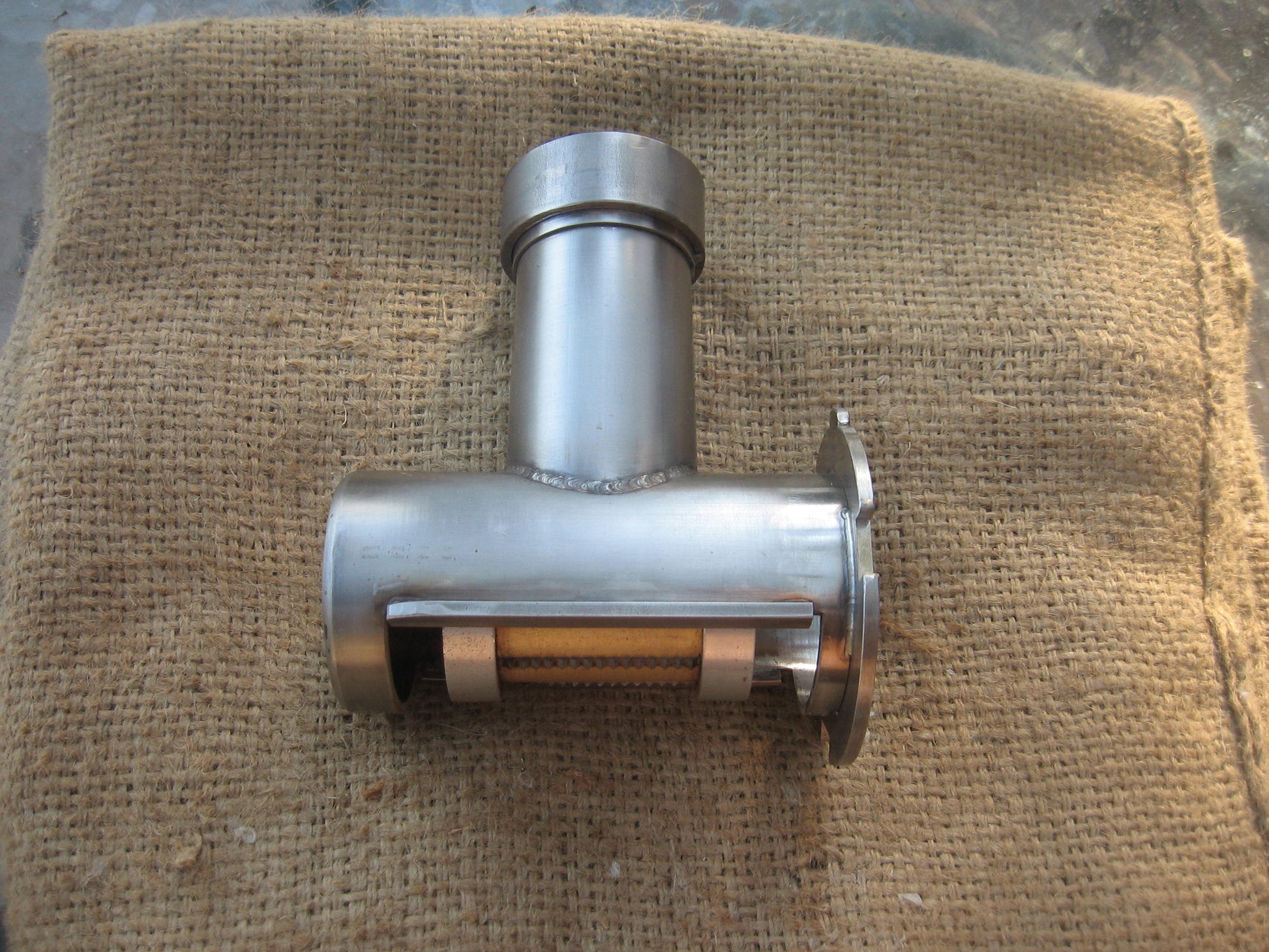 A stainless steel and brass Deluxe Cracker for use with a juicer, placed on a burlap sack.